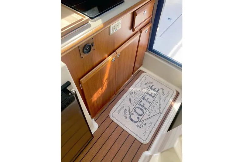 Slide: The Image of 2021 Ranger Tugs R-25 interior with wooden cabinetry and a coffee-themed mat. - 20