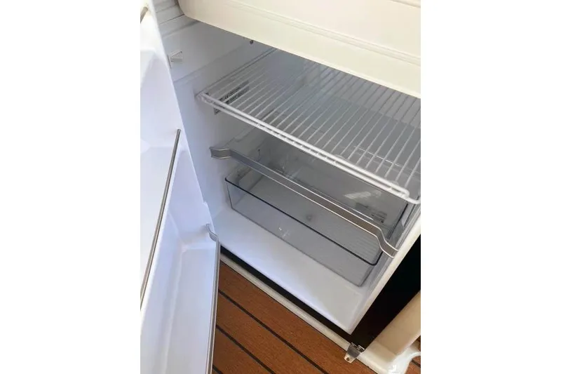 Slide: The Image of Empty refrigerator inside a 2021 Ranger Tugs R-25 boat, featuring wire shelving and a clear drawer. - 22