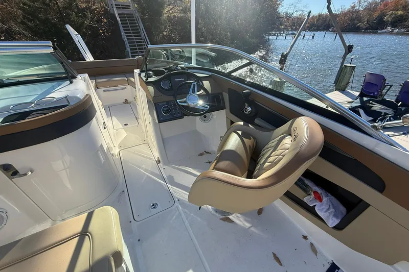 Slide: The Image of 2015 Sea Ray 240 Sundeck interior with steering wheel and seating, docked by a scenic lake. - 10