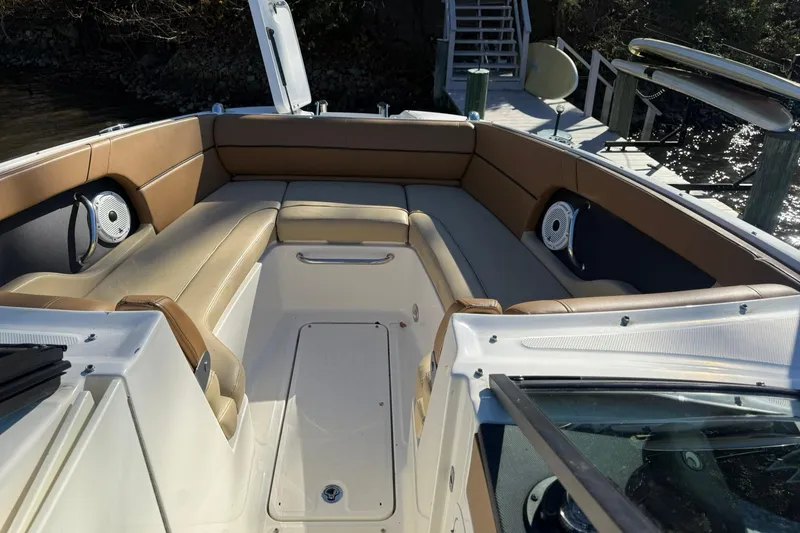 Slide: The Image of 2015 Sea Ray 240 Sundeck interior with tan seating and speakers, docked by the water. - 16