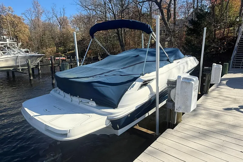 Slide: The Image of 2015 Sea Ray 240 Sundeck boat docked with cover, surrounded by autumn trees. - 2
