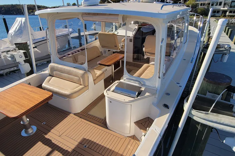 Slide: The Image of 2017 MJM 40z Downeast yacht with elegant seating and wooden tables docked by the water. - 10