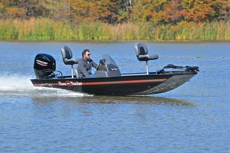 The Image of 2024 Bass Tracker Classic boat cruising on a lake with autumn foliage in the background. - 1