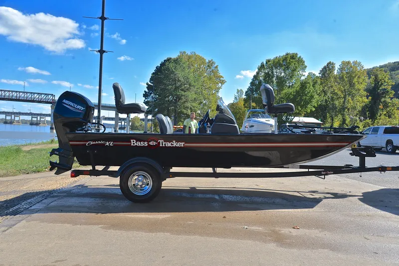 Slide: The Image of 2024 Bass Tracker Classic boat on trailer by riverside, under clear blue sky. - 15