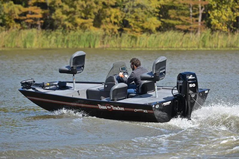 Slide: The Image of 2024 Bass Tracker Classic boat cruising on a lake with lush greenery in the background. - 6