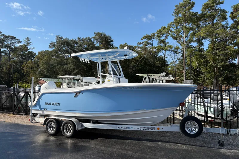 Slide: The Image of 2024 Blackfin 222CC boat on trailer, parked outdoors, surrounded by trees and other boats. - 0