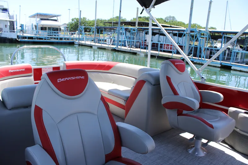 Slide: The Image of 2024 Berkshire 24RFX LE pontoon boat interior with red and gray seating at marina. - 5
