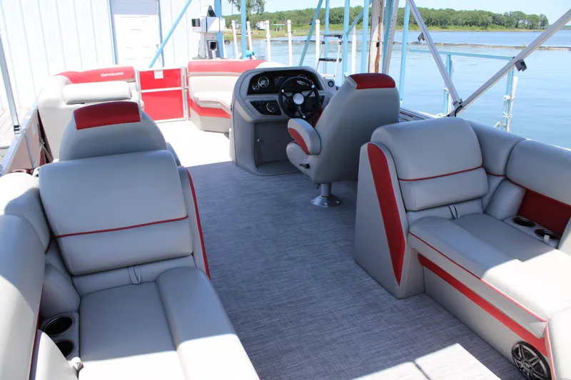 Slide: The Image of 2024 Berkshire 24RFX LE pontoon boat interior with gray and red seating, steering console, and lake view. - 6