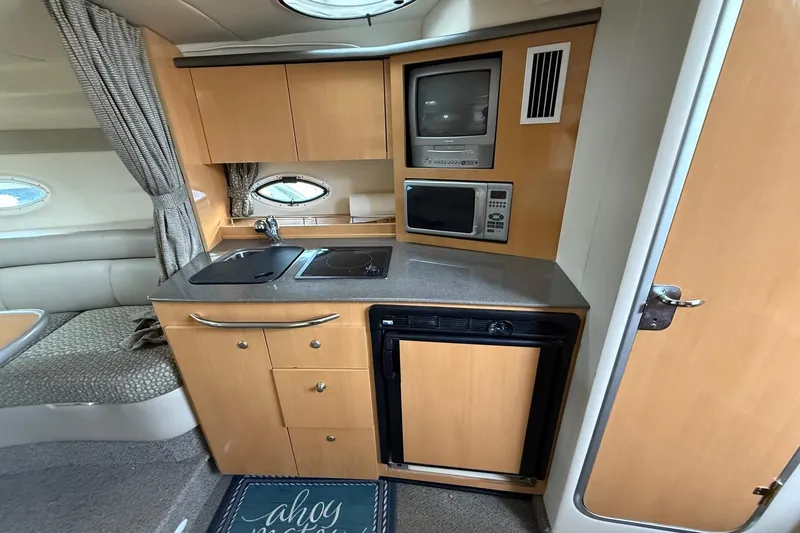 Slide: The Image of 2004 Maxum 3100 SE boat interior with kitchenette, featuring sink, stove, microwave, and fridge. - 14