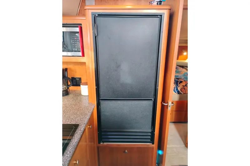 Slide: The Image of 2004 Meridian 459 Motoryacht interior with black refrigerator and wooden cabinetry. - 54