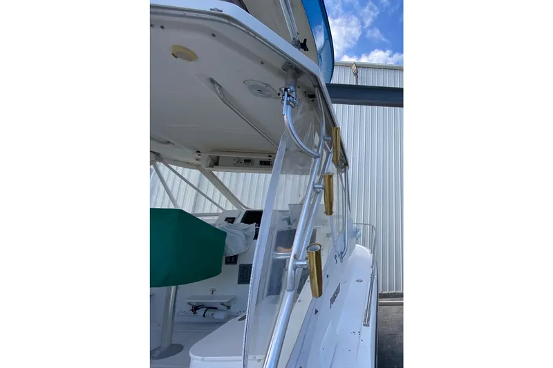 Slide: The Image of 2001 Pursuit 3000 Offshore boat with rod holders and covered cockpit, docked near a metal building. - 12