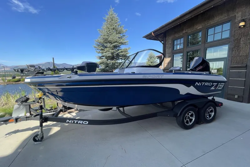 The Image of 2026 Nitro ZV19 Sport Pro boat on trailer, parked near a lake and building. - 0