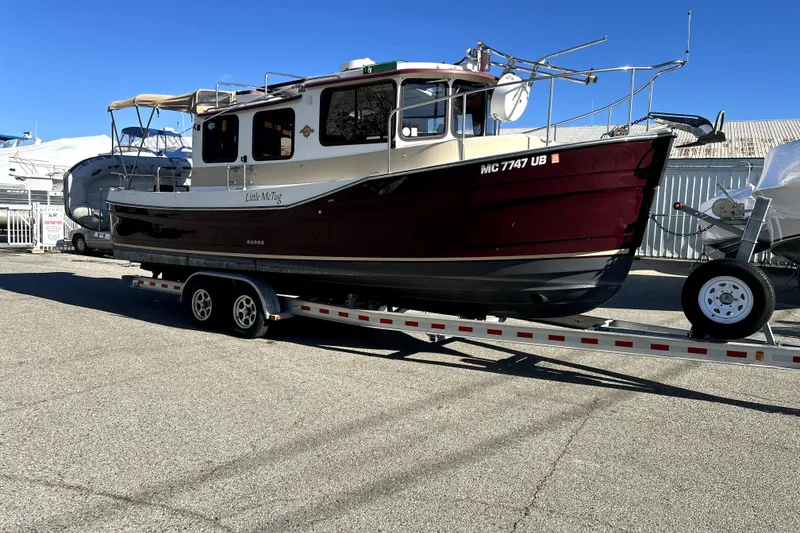 The Image of 2013 Ranger Tugs R-27 boat on trailer, maroon and white, parked outdoors. - 0