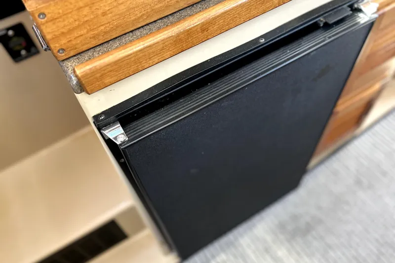 Slide: The Image of 2013 Ranger Tugs R-27 interior showing a compact black refrigerator and wooden cabinetry. - 15