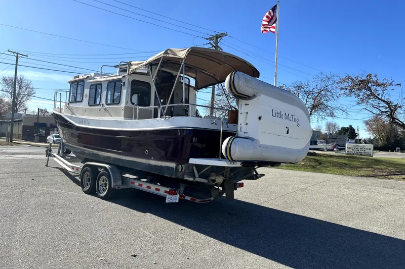 Slide: The Image of 2013 Ranger Tugs R-27 boat on trailer, named "Little McTug," with American flag in background. - 3