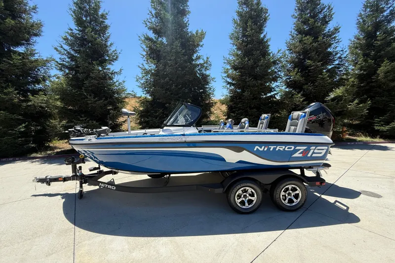 The Image of 2026 Nitro ZV19 Sport Pro boat on trailer, parked outdoors with trees in background. - 0