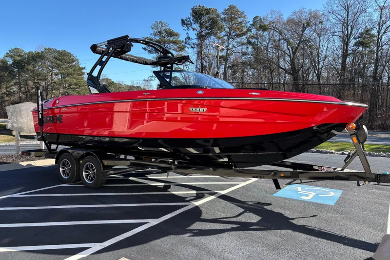 Slide: The Image of Red 2026 Supreme S240 boat on trailer in parking lot, surrounded by trees. - 2