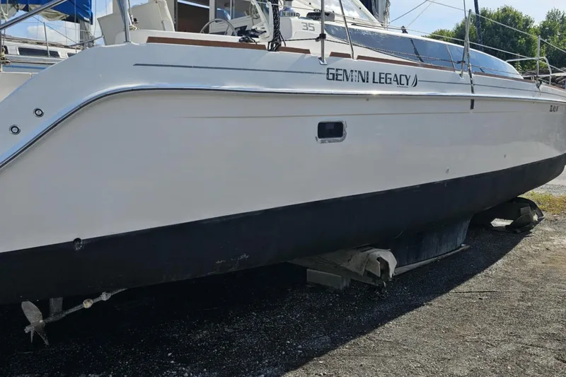 Slide: The Image of 2014 Gemini Legacy 35 catamaran on land, white hull, black bottom, outdoor setting. - 6