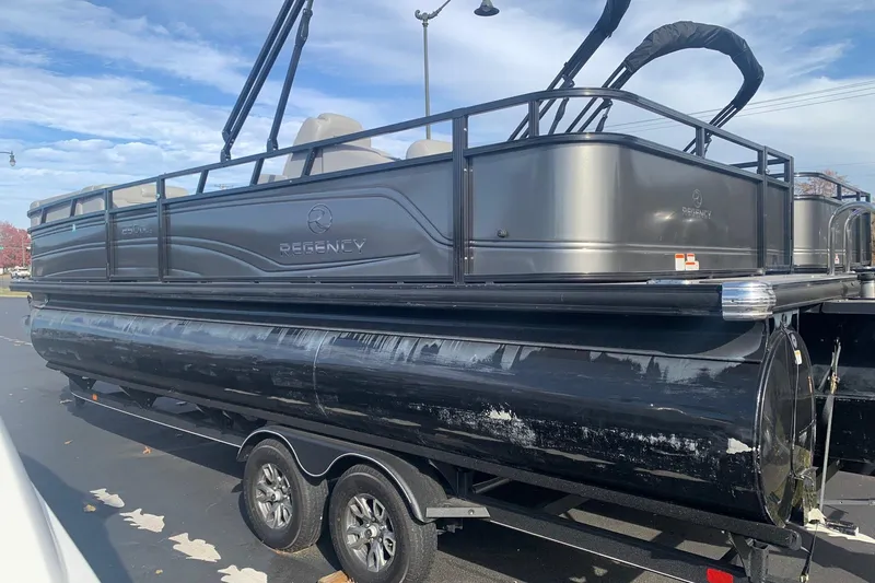 The Image of 2024 Regency 250 DL3 pontoon boat on trailer, sleek black design, parked outdoors. - 1