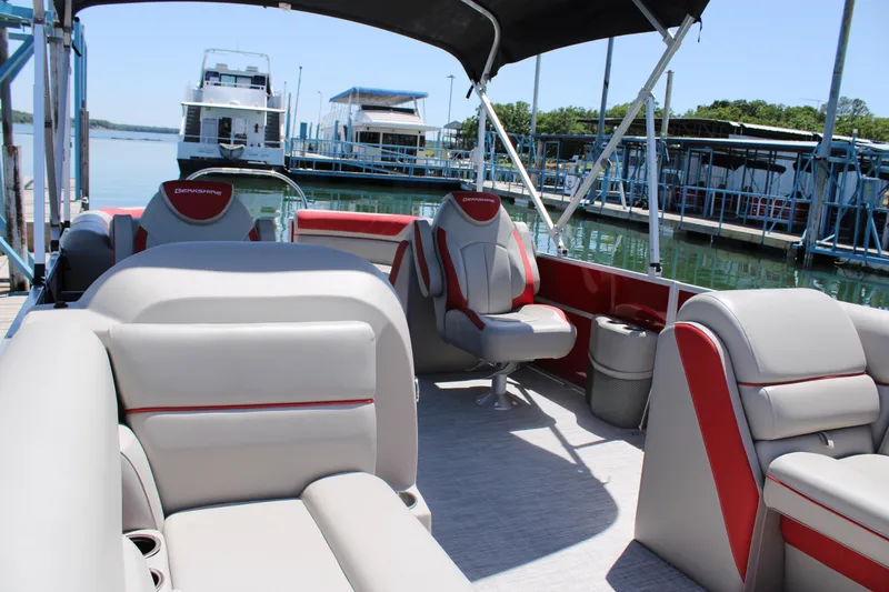 Slide: The Image of 2024 Berkshire 24RFX LE pontoon boat interior with red and gray seating at a marina. - 5