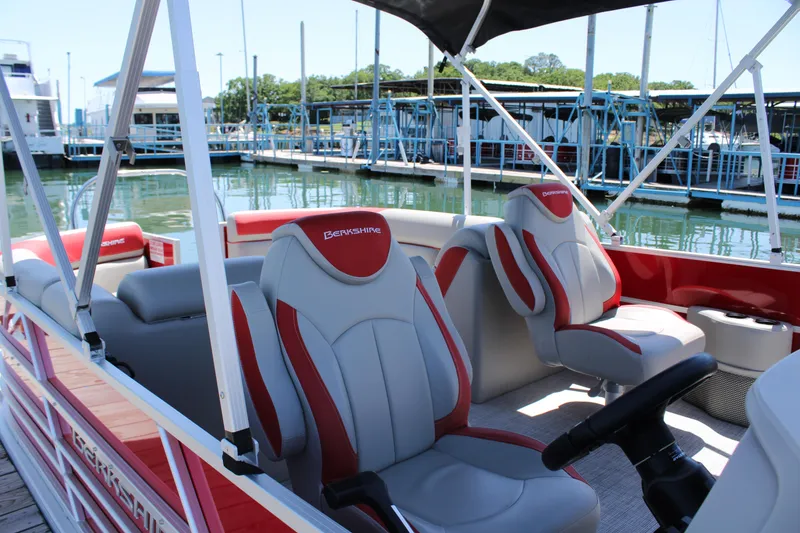 Slide: The Image of 2024 Berkshire 24RFX LE pontoon boat interior with red and gray seating at a marina. - 6