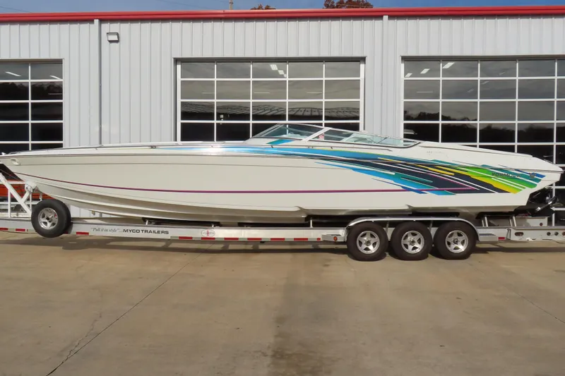 The Image of 1999 Formula 382 FASTech speedboat on trailer, vibrant graphics, parked outside a garage. - 0