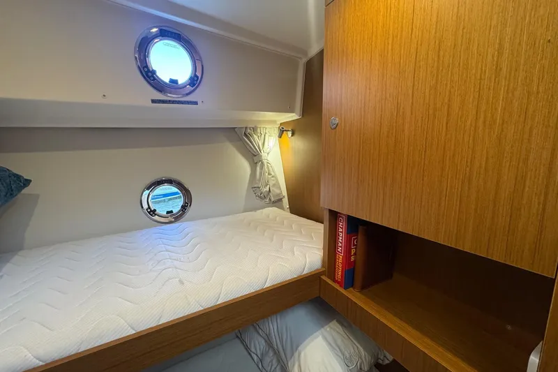 Slide: The Image of 2023 Beneteau Swift Trawler 35 cabin with cozy bed, portholes, and wooden storage. - 56