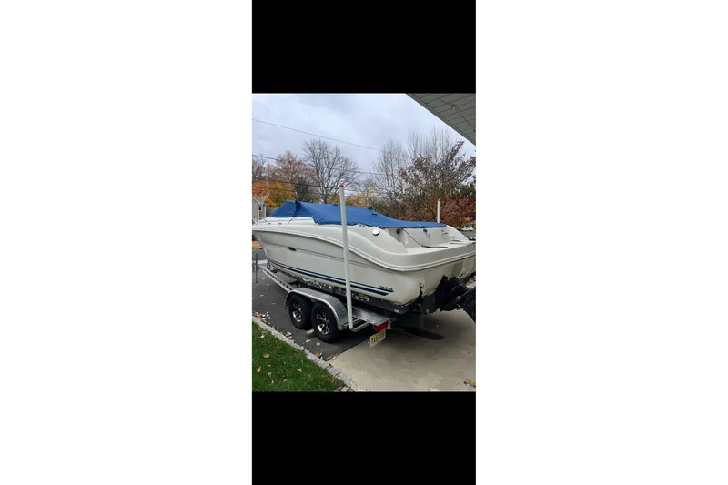 Slide: The Image of 2004 Sea Ray 215 Weekender boat on trailer, covered with blue tarp, parked outdoors. - 3