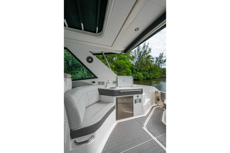 Slide: The Image of 2023 Sea Ray Sundancer 320 Outboard interior with seating and kitchenette, near lush greenery. - 44