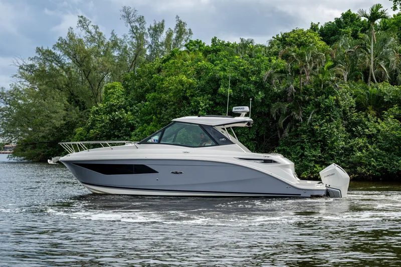 Slide: The Image of 2023 Sea Ray Sundancer 320 Outboard cruising on a serene waterway, surrounded by lush greenery. - 67