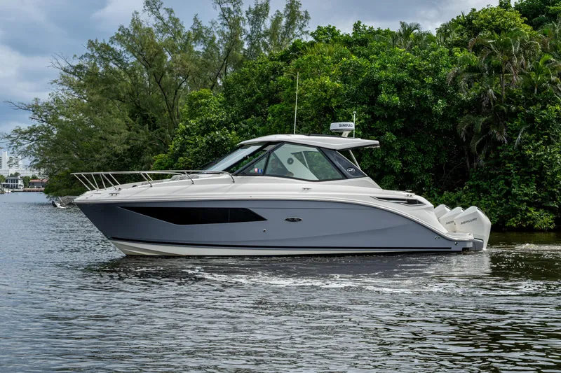 Slide: The Image of 2023 Sea Ray Sundancer 320 Outboard cruising on a serene waterway, surrounded by lush greenery. - 68