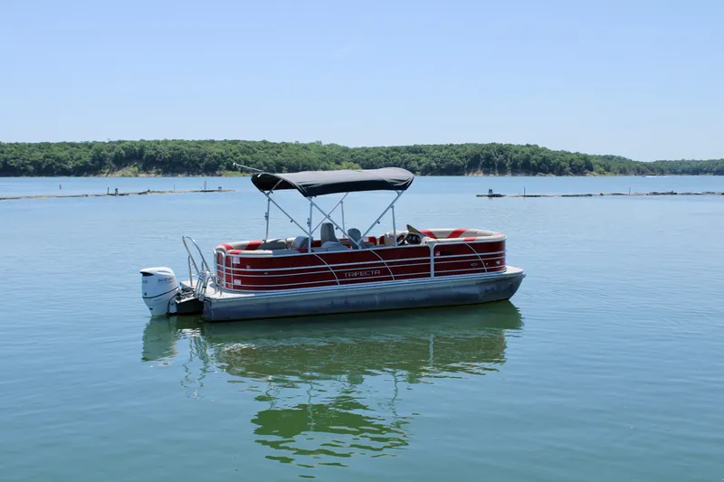 Slide: The Image of 2022 Trifecta 24RFLE pontoon boat on a calm lake with scenic background. - 2