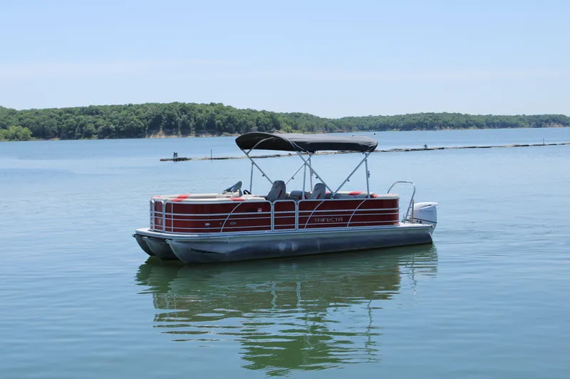 The Image of 2022 Trifecta 24RF LE pontoon boat on a serene lake with forested shoreline. - 1
