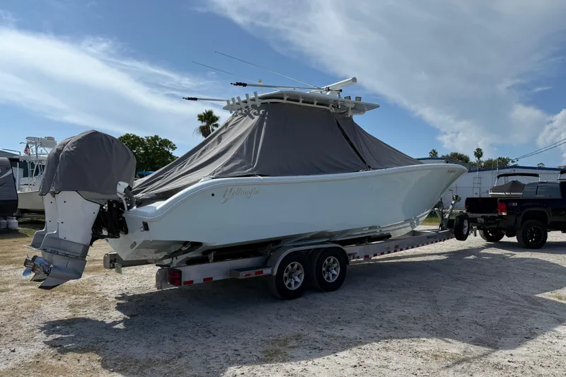 Slide: The Image of 2018 Yellowfin 32 Offshore boat on trailer, covered, with truck nearby under blue sky. - 105