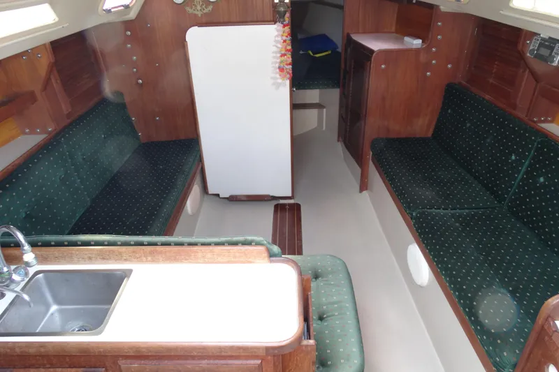 Slide: The Image of 1988 Catalina MKll yacht interior with green upholstery, wooden cabinetry, and compact kitchen area. - 15