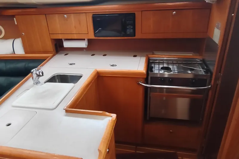Slide: The Image of 2003 Hunter 356 yacht kitchen with sink, stove, and microwave in wooden cabinetry. - 30