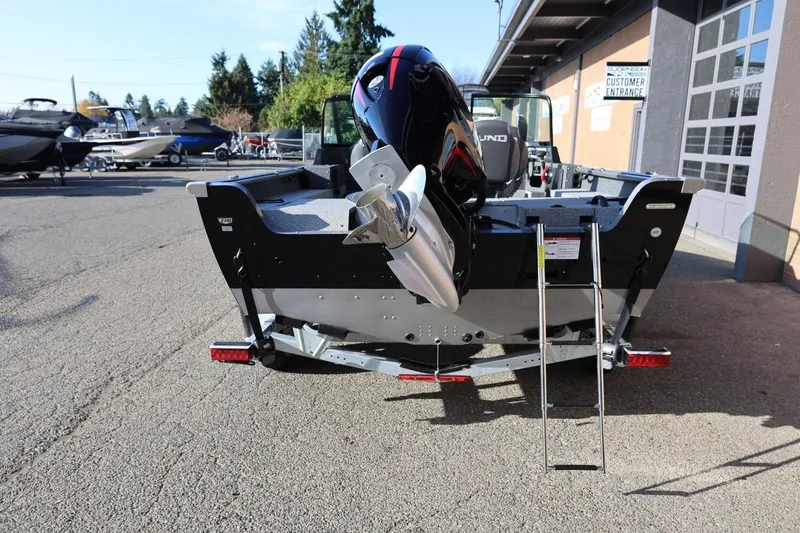 Slide: The Image of 2026 Lund 1875 Impact XS Sport boat with outboard motor and ladder, parked outdoors. - 3