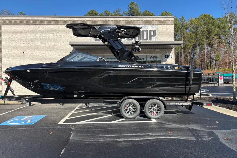 The Image of 2026 Centurion Ri245 boat on trailer, parked in front of a shop, sunny day. - 0