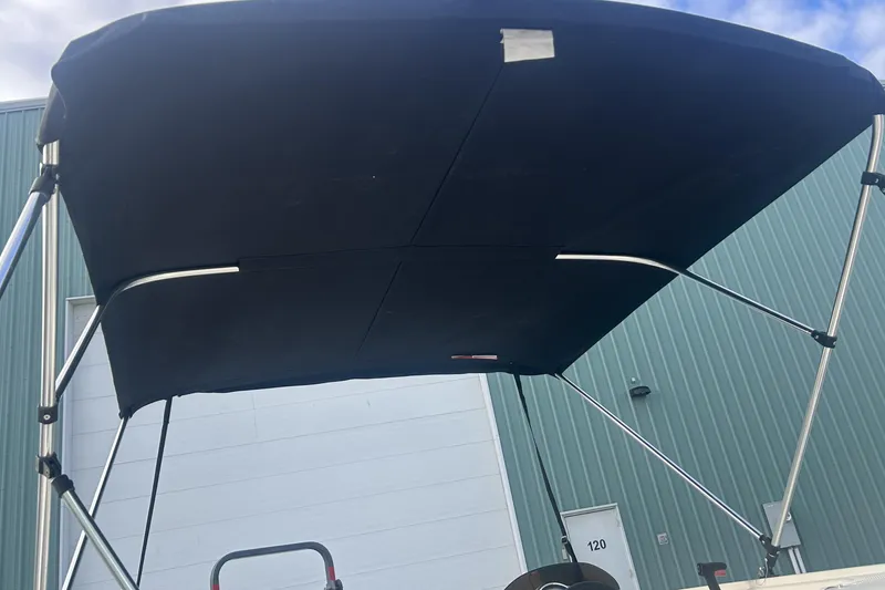 Slide: The Image of 2016 Bayliner Element XL boat with black bimini top, parked near a green building. - 24