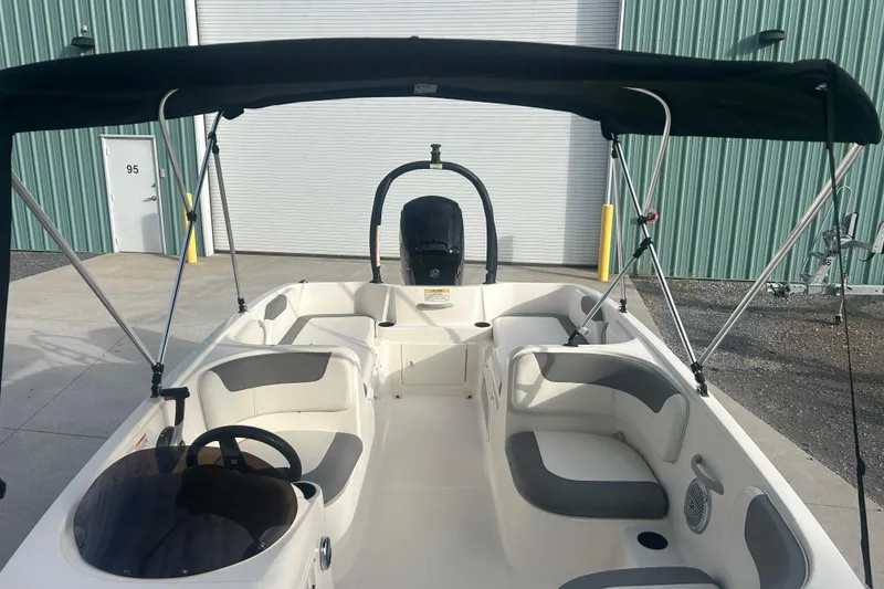 Slide: The Image of 2016 Bayliner Element XL boat interior with seating and canopy, parked near a green building. - 25