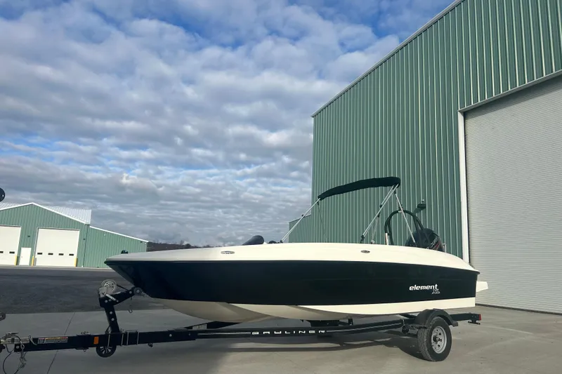 Slide: The Image of 2016 Bayliner Element XL boat on trailer, parked near large green building. - 60