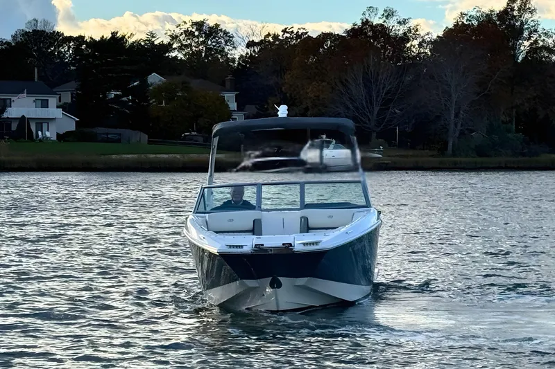 Slide: The Image of 2019 Cobalt 25SC boat cruising on a serene lake with houses in the background. - 6