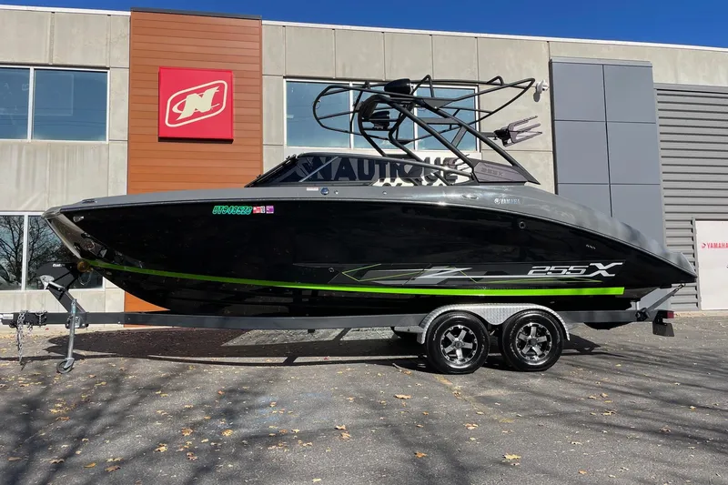 The Image of 2021 Yamaha Boats 255XD on trailer, parked outside dealership, black with green accents. - 1