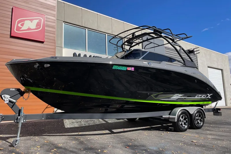 Slide: The Image of 2021 Yamaha Boats 255XD in black with green accents on a trailer outside a dealership. - 2
