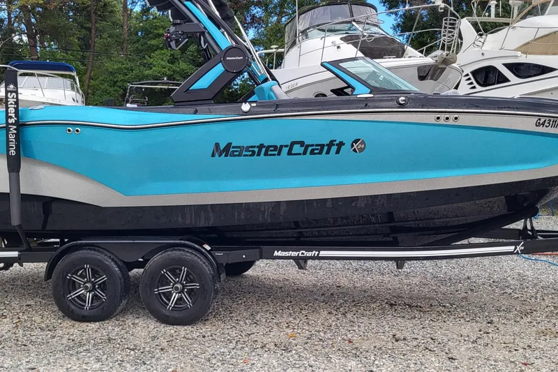 Slide: The Image of 2022 MasterCraft X24 boat on trailer, vibrant blue, parked near other boats. - 0
