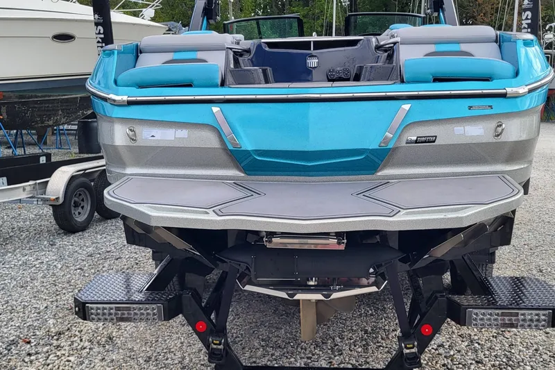 Slide: The Image of 2022 MasterCraft X24 boat, blue and silver, rear view on gravel lot. - 15