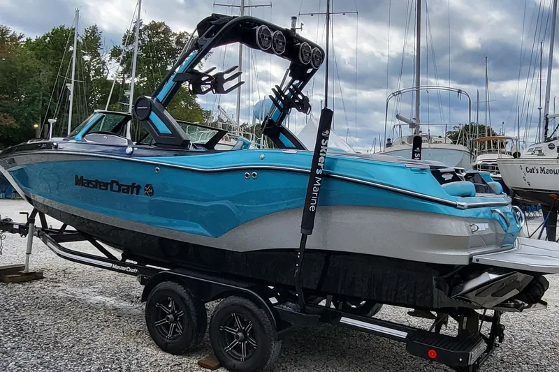 Slide: The Image of 2022 MasterCraft X24 boat on trailer, vibrant blue, docked at marina. - 2