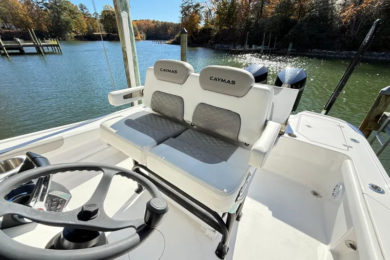 Slide: The Image of 2023 Caymas 281 HB boat interior with dual seats and steering wheel, docked by a scenic lake. - 21