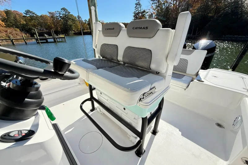 Slide: The Image of 2023 Caymas 281 HB boat interior with cushioned seating and steering wheel, docked by a scenic lake. - 22