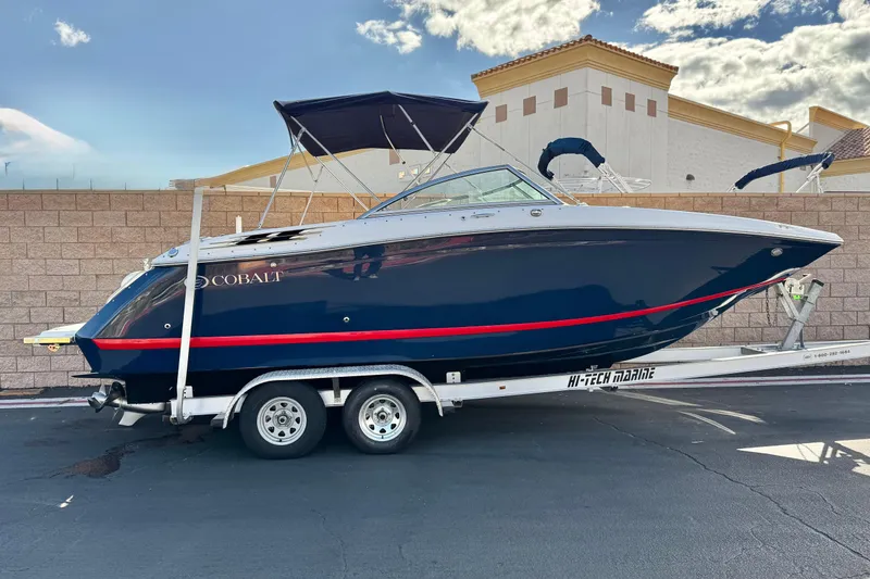 The Image of 2014 Cobalt 24SD boat on trailer, navy blue with red stripe, parked outdoors. - 0